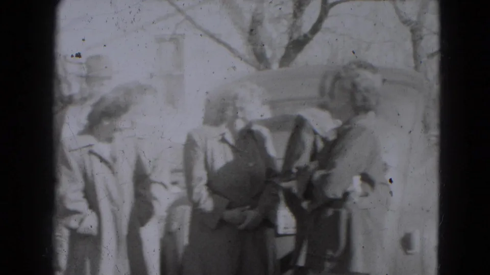 Adults in 1940s coats and hats stand together near a vehicle in the Lincoln, Nebraska home-movie scene.