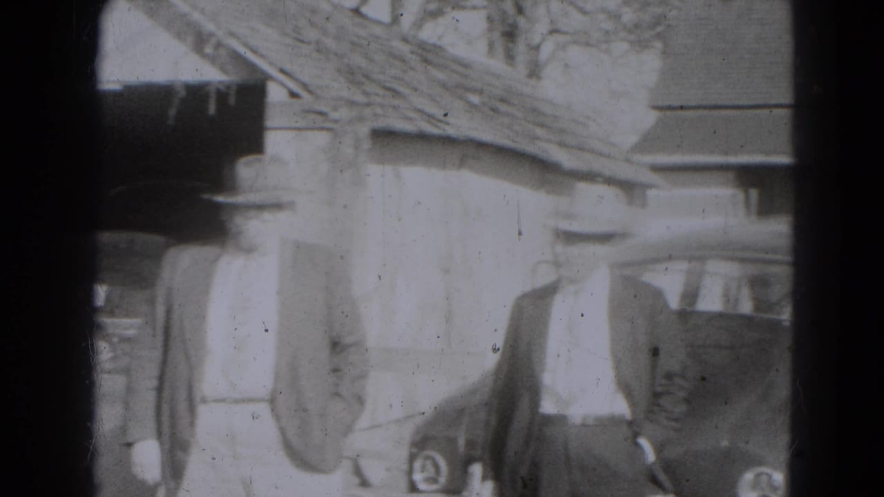 Adults in coats and hats stand near parked rounded cars outside a building.