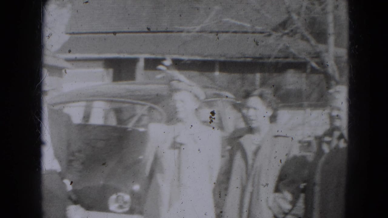 Several adults stand beside a rounded car near a building entrance.