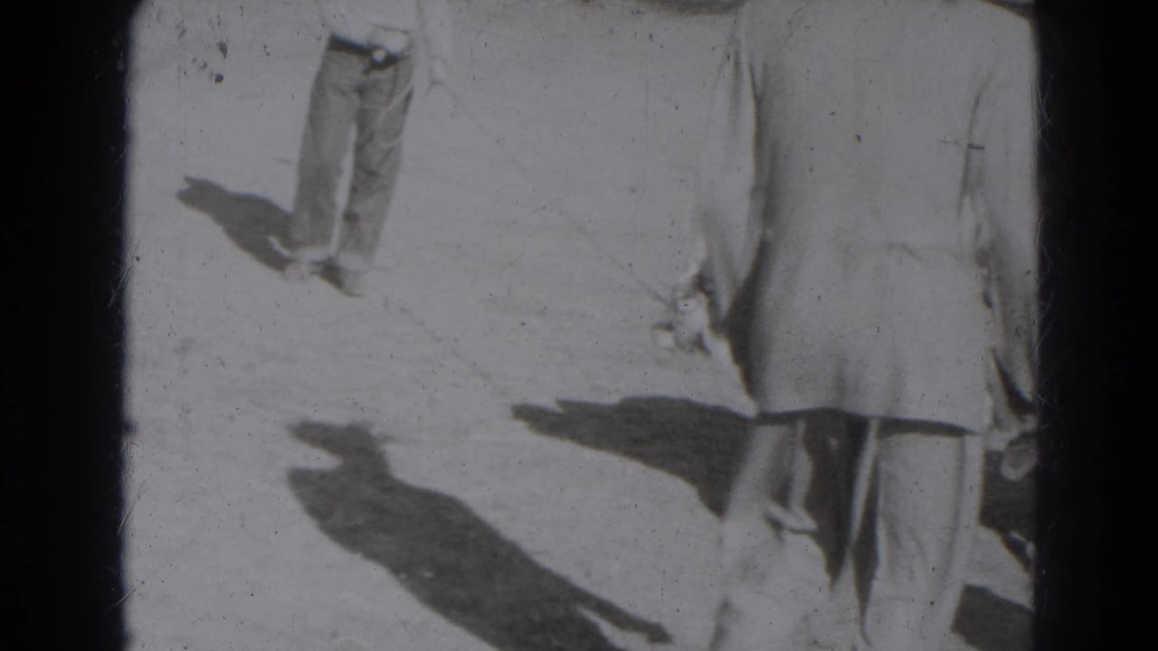 Black-and-white frame of adults on a bright open surface with long shadows.