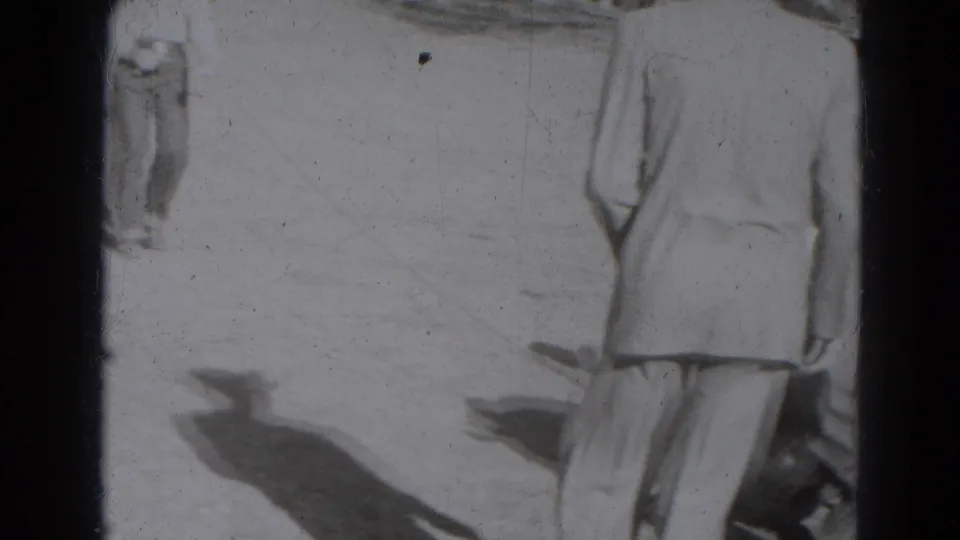 Black-and-white 8mm frame from Lincoln, Nebraska, 1947, with a cropped adult in light clothing on bright ground.
