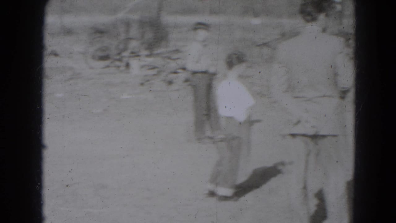 A small group watches in a dusty Lincoln, Nebraska yard, with a smaller participant visible near adults in the 1947 home-movie frame.