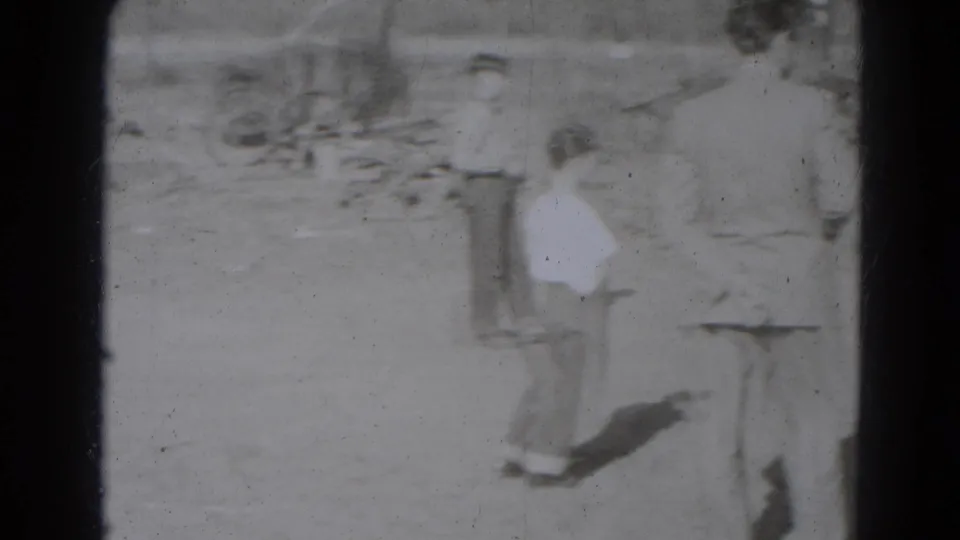 A small group watches in a dusty Lincoln, Nebraska yard, with a smaller participant visible near adults in the 1947 home-movie frame.