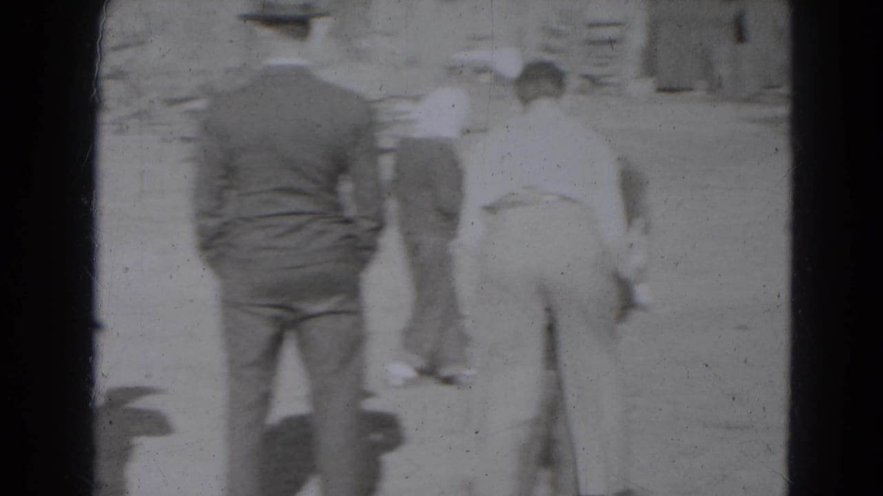 Adults in 1940s dress stand with their backs to the camera while watching activity in an outdoor Lincoln, Nebraska yard.
