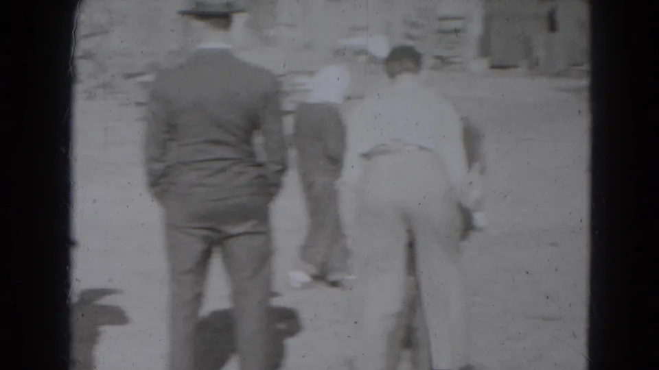 Adults in 1940s dress stand with their backs to the camera while watching activity in an outdoor Lincoln, Nebraska yard.
