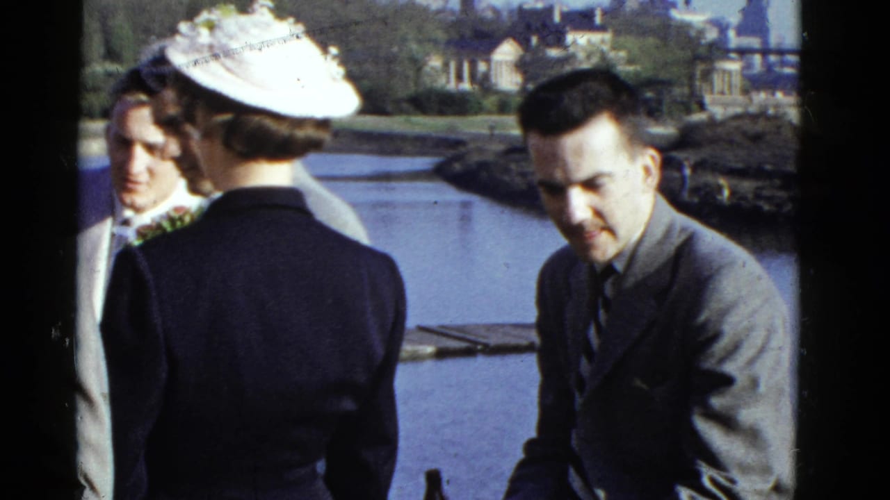 1951 Boston waterfront home-movie frame showing formally dressed adults conversing near water and distant buildings.