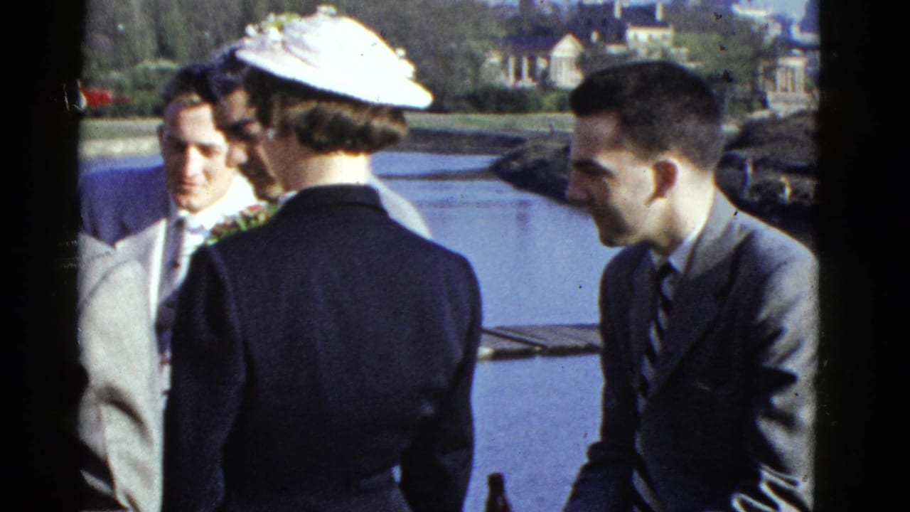 A woman in a white hat faces suited men beside a body of water.