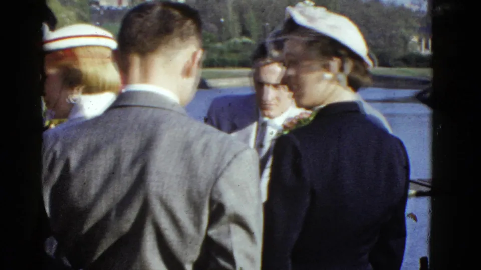 1951 Boston waterfront frame with suited adults and a woman in a white hat gathered in bright daylight.