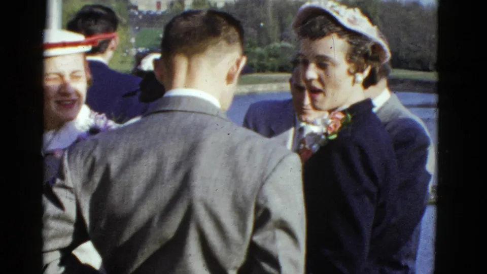 1951 Boston home-movie frame showing well-dressed adults talking outdoors in a park-like setting.