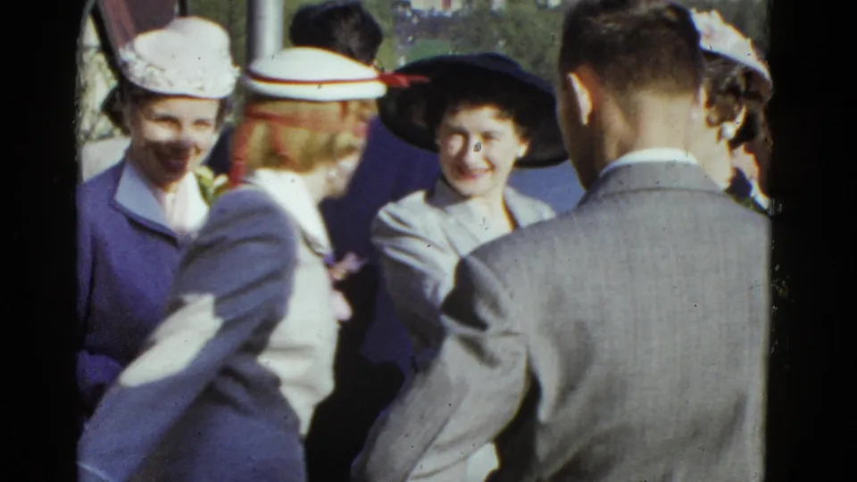 1951 Boston home-movie frame showing women in period hats smiling during an outdoor social gathering.