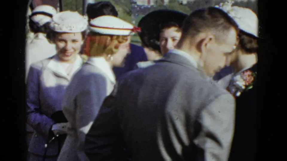Candid 1951 Boston frame of a suited man and hat-wearing women gathered outdoors in bright sun.