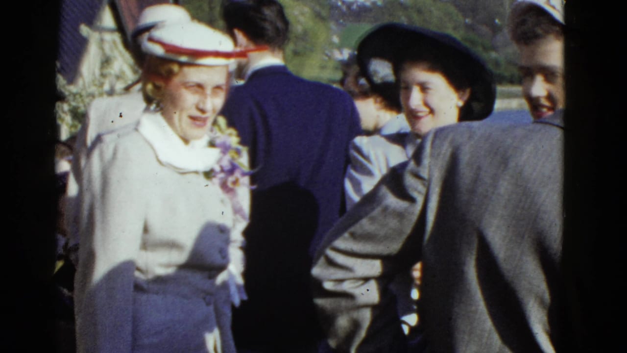 1951 Boston home-movie frame showing women in mid-century formal suits and hats conversing outdoors at a gathering.