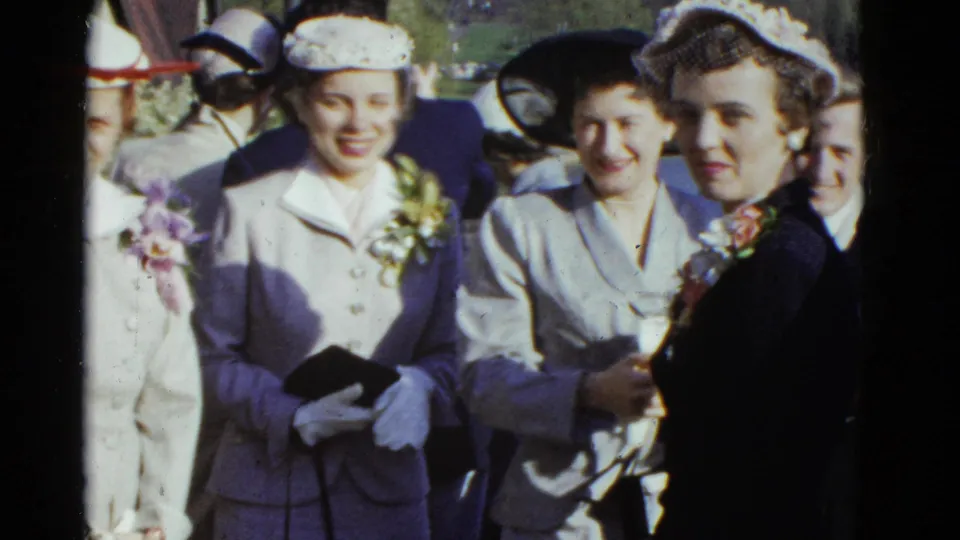 1951 Boston frame of women in suits, hats, gloves, and corsages standing in a formal outdoor gathering.