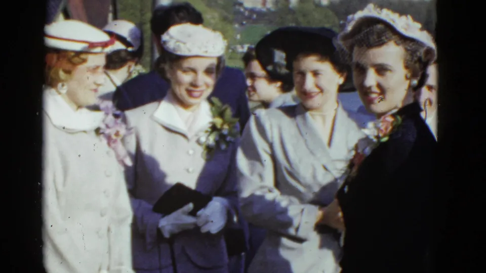 Women in 1950s hats, gloves, coats, and corsages stand close together outdoors in Boston, according to clip metadata.