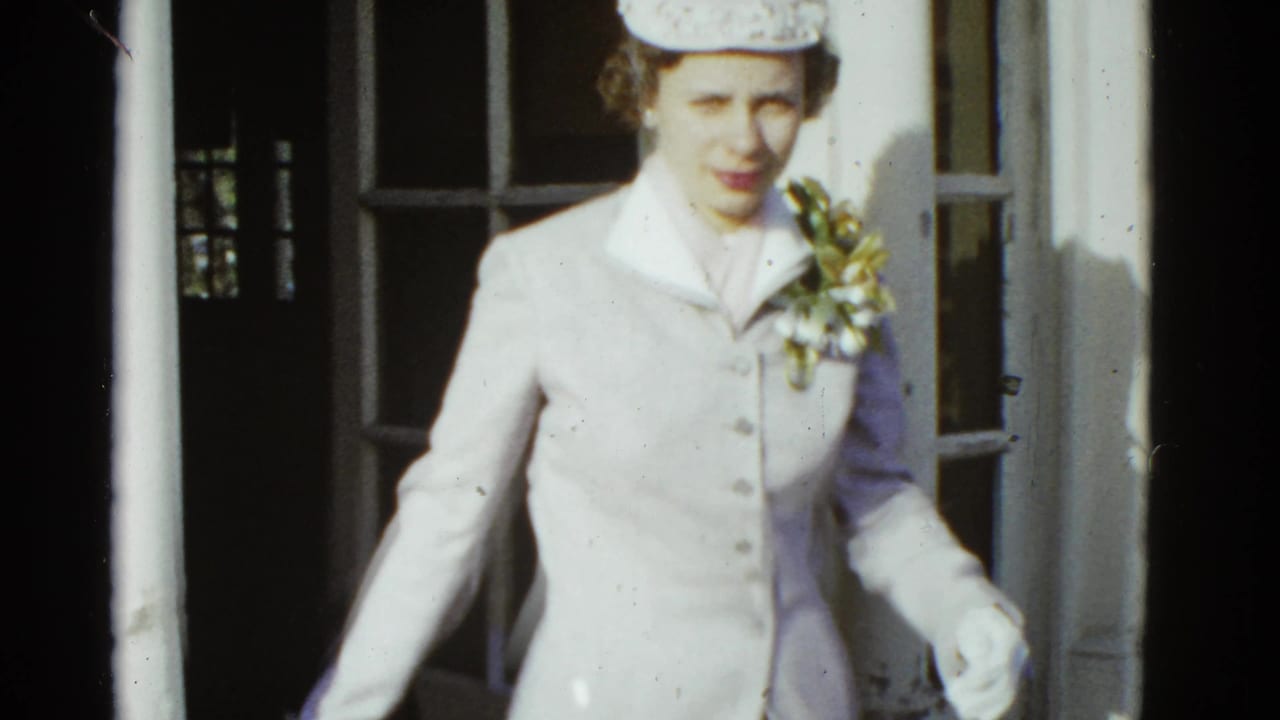 In 1951 Boston home-movie footage, a woman in a pale outfit and patterned hat emerges from a brick building doorway.
