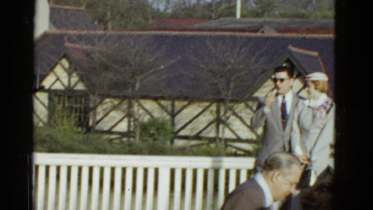 In 1951 Boston home-movie footage, a man in a light suit and sunglasses stands beside a woman in white near a railing and timbered building.
