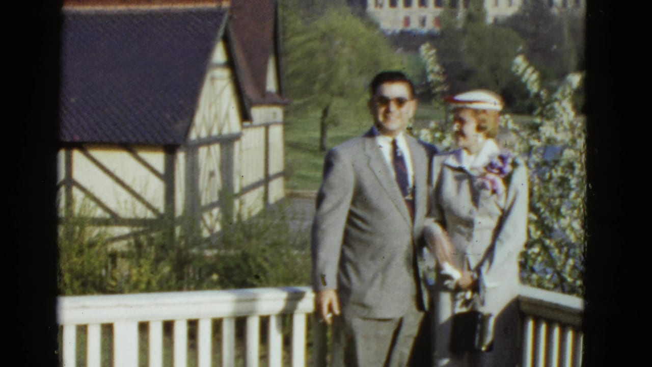 Couple faces the camera near a railing with a timber-framed building behind them.