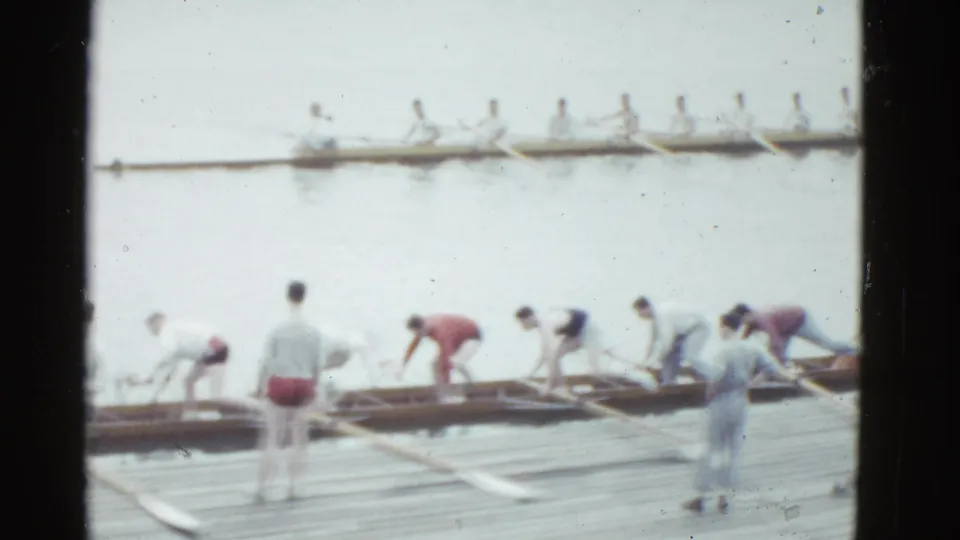 1951 Boston home-movie view of rowers and observers on a wooden dock with long shells and oars extending across the water.