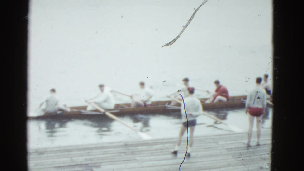 Crew members sit in a shell while two men stand on the dock nearby.