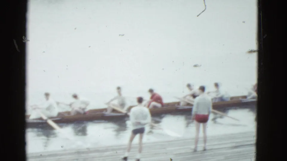Boston 1951 home-movie frame of men around a rowing shell, with oars extended and dockside figures watching the practice.