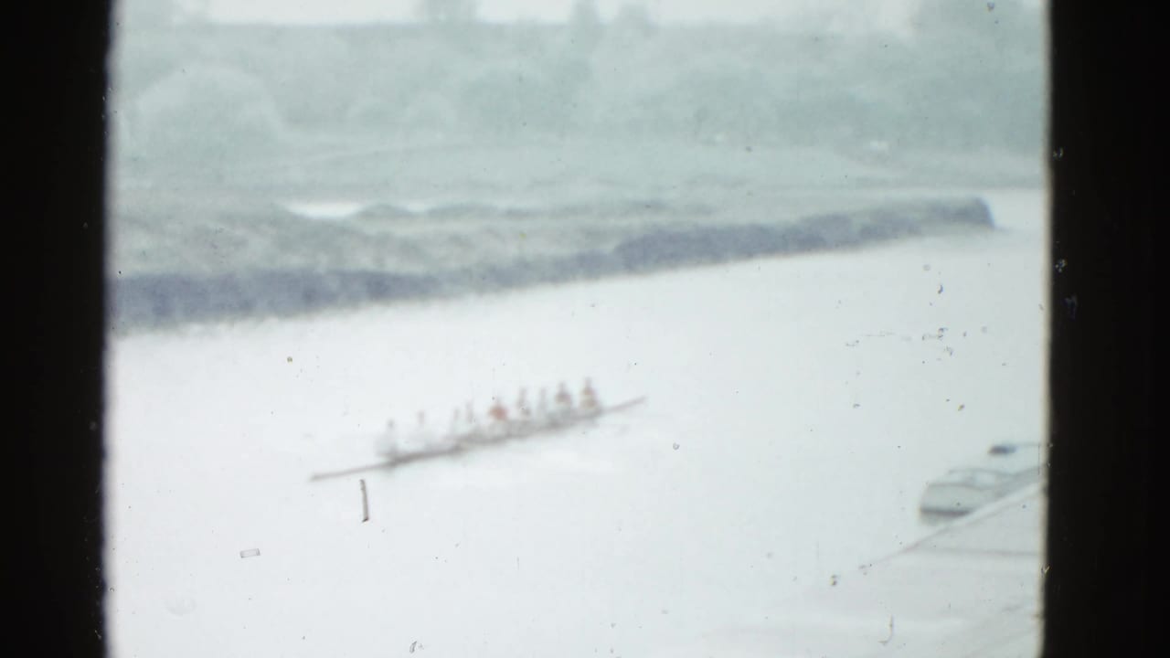 Rowing crew seen through a dark window frame on a wide river.
