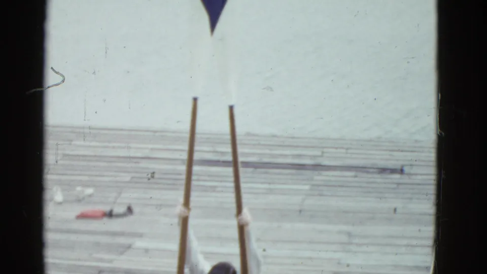 Boston 1951 home-movie frame showing long rowing oars on a wooden pier near the river, with a cropped person at the lower edge.