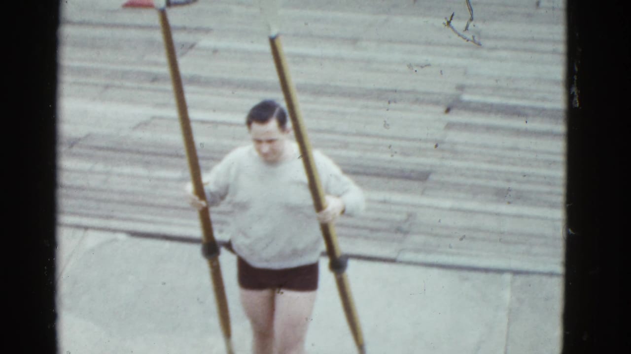 Boston 1951 frame of a man on a wooden pier holding two long oars, preparing near the riverfront.