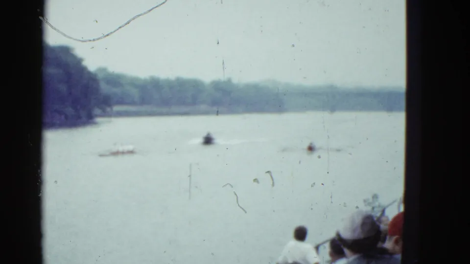 1951 Boston home-movie view of sculls on a broad river, with a small motorboat and spectators seen from behind near the lower frame.