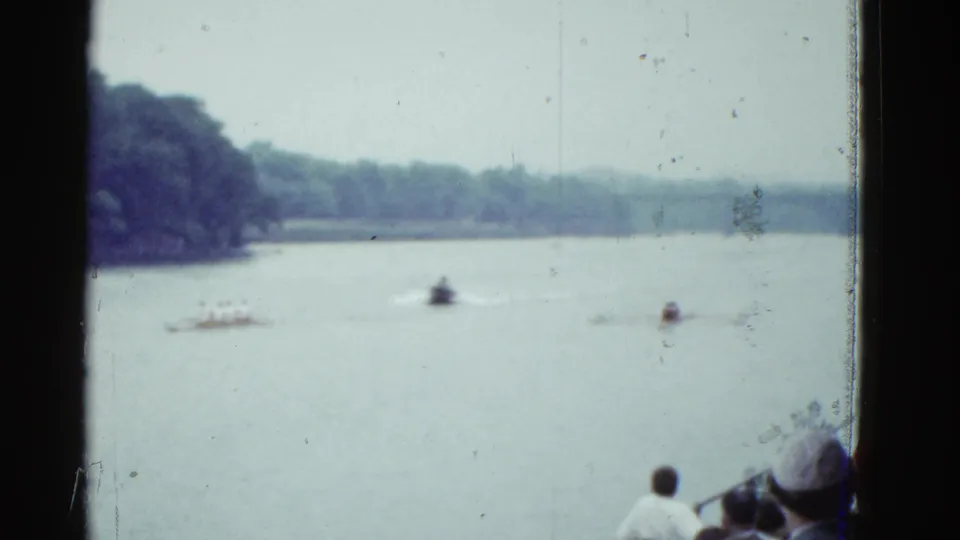 Boston-area 1951 rowing race footage shows distant sculls and a motorboat on the water, with spectators partly visible at the riverbank.