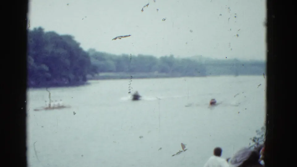 Soft 8mm frame of the 1951 Boston sculling race, with boats spread across the river and a spectator seen from behind in the foreground.