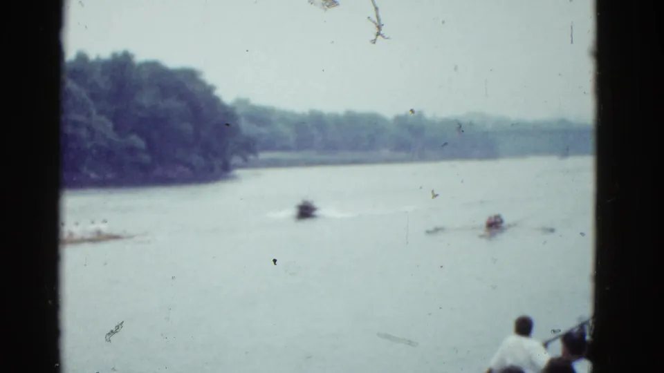 Final 1951 Boston home-movie frame shows a sculling race from a spectator position, with boats on the river and trees along the far bank.
