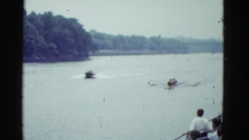 A Boston river race appears in soft 8mm color, with a motorboat wake, rowing crew, wooded bank, and shore spectators.