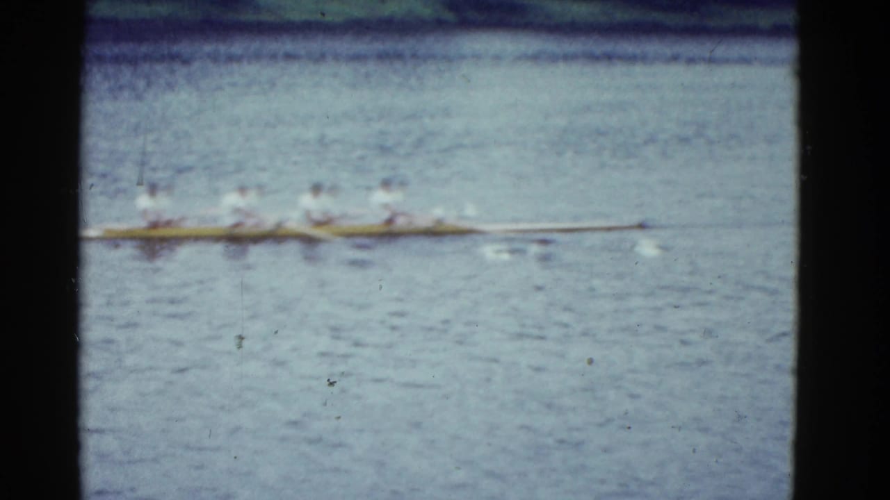 Distant rowers in a long shell crossing rippled water.