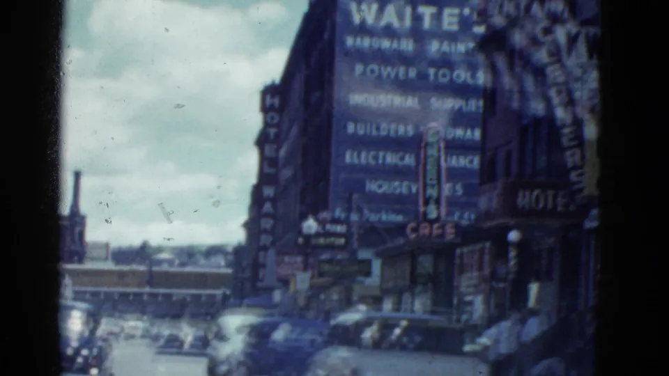 A mid-century city street view shows cars, storefronts, and prominent hotel and trade-service signage in the Boston-labeled footage.