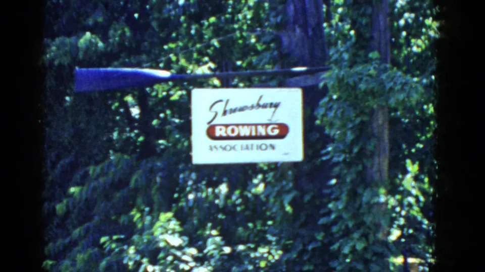 1951 8mm frame of a Shrewsbury Rowing Association sign and mounted blue oar in a leafy Boston-area outdoor setting.