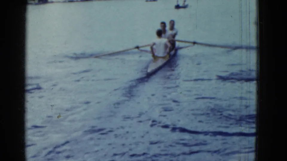 A 1951 8mm view of the rowing shell receding across open water, with a small distant boat near the top of frame.