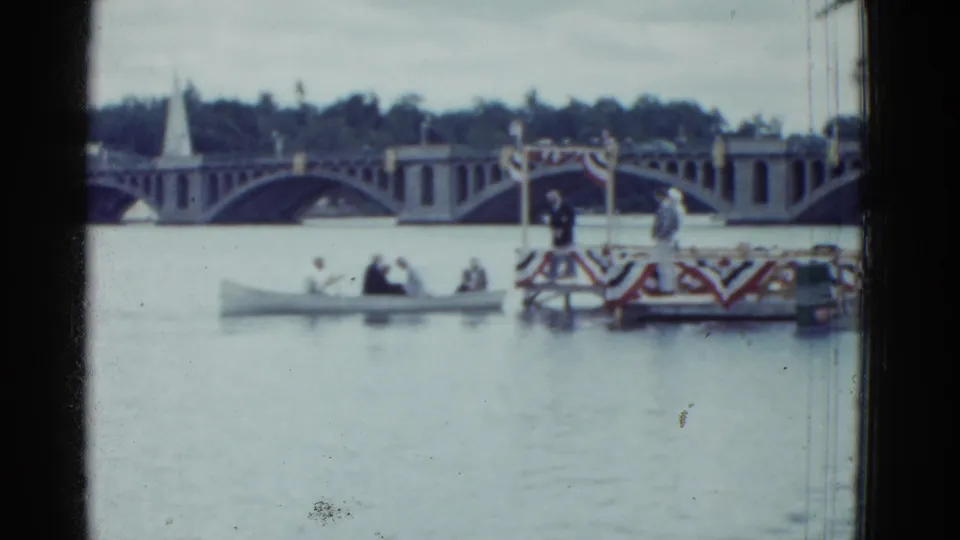 1951 Boston home-movie view of a small boat on the river near a patriotic platform, with the bridge and distant spire behind.