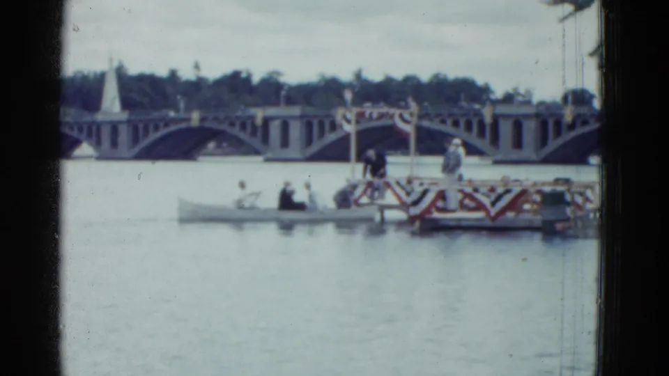 1951 Boston 8mm frame showing rowers near a decorated finish area on a river, with an arched bridge and trees in the background.