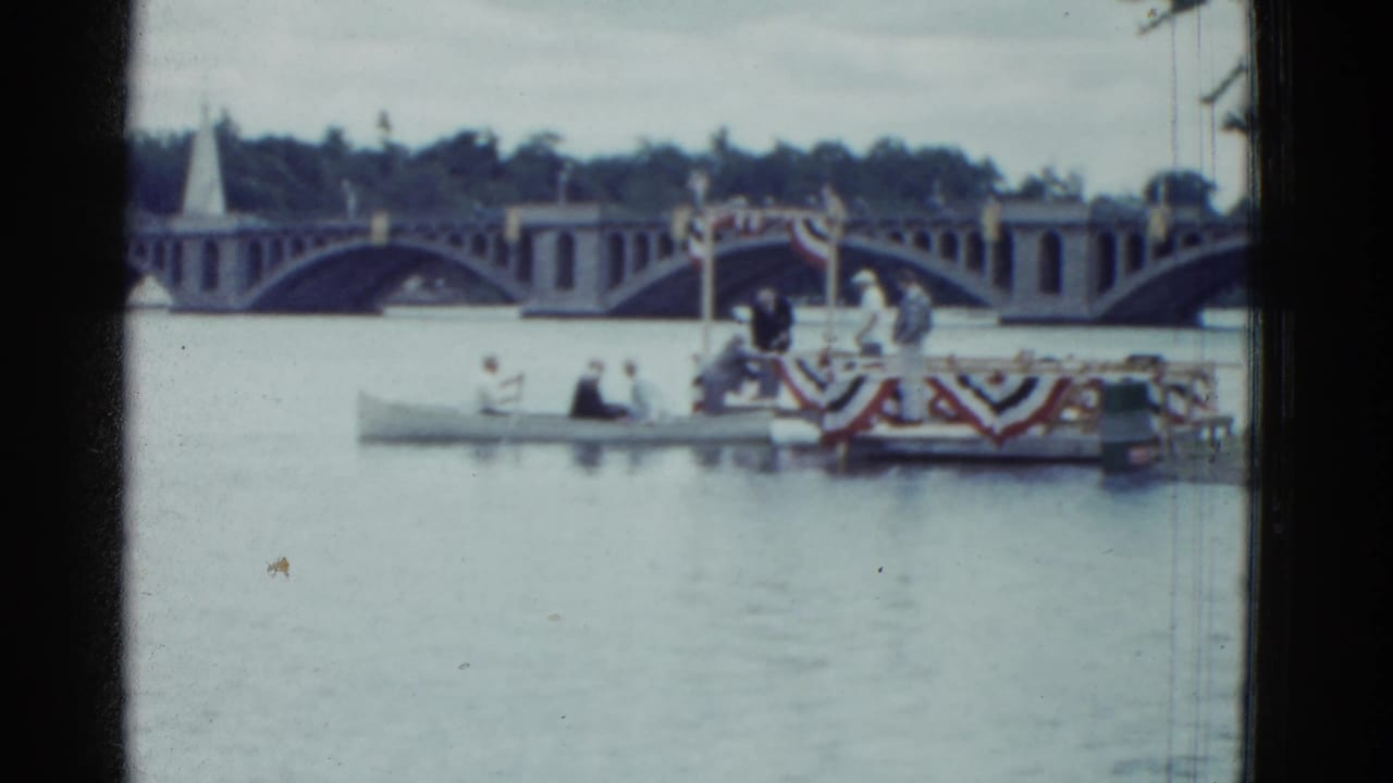 Small boat and decorated platform near the finish area, with people standing and sitting on the river.