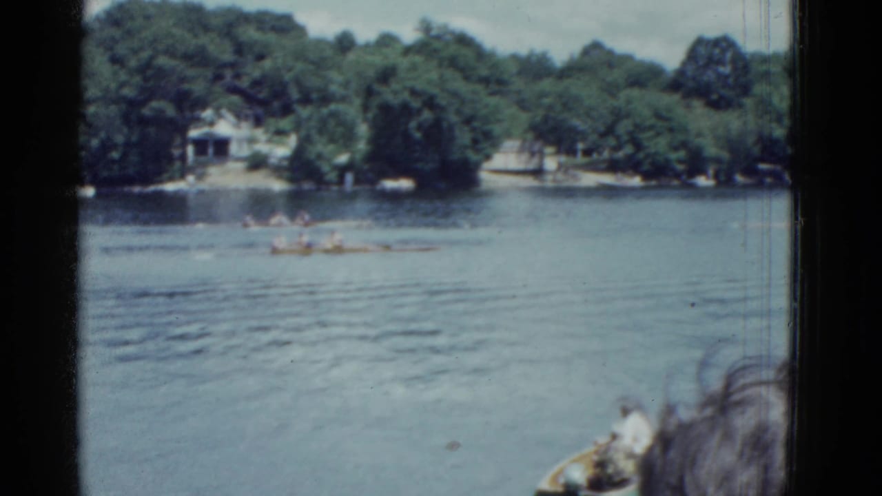 Rowers continue across the lake as a small boat and foreground spectator appear at lower right.