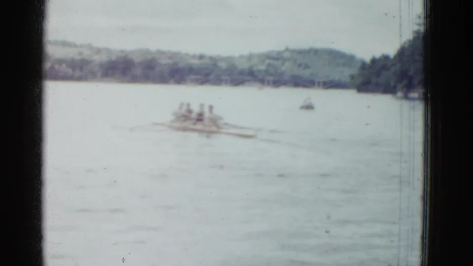 Distant 1951 Boston-area rowing scene with a shell on open water, soft focus, and a tree-lined far bank.