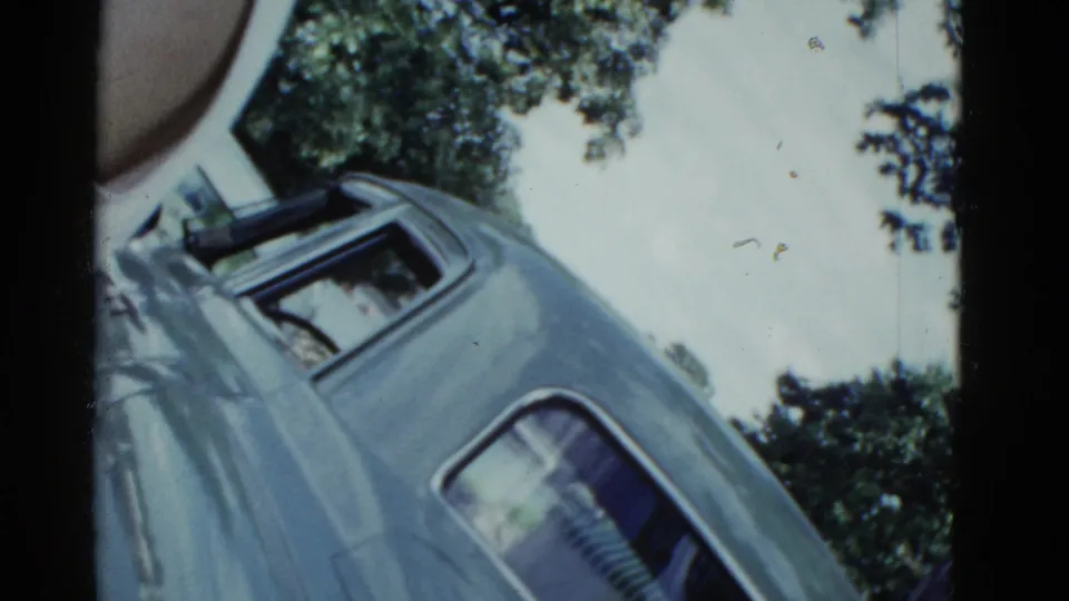 1951 Boston home-movie frame showing a tilted low-angle view of a light blue classic car under leafy trees.