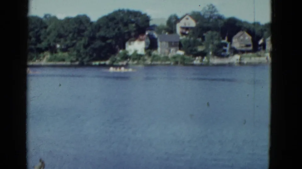 1951 Boston-area lake view showing calm water, a small boat, and houses along a tree-lined far shore.