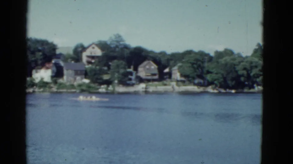 1951 Boston-area 8mm frame showing a small boat crossing a wide river below distant homes and trees.