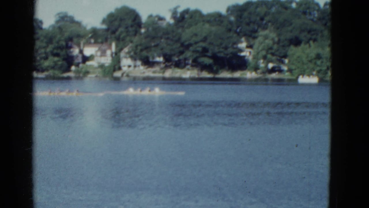 Long rowing boat with several rowers moving across open water.