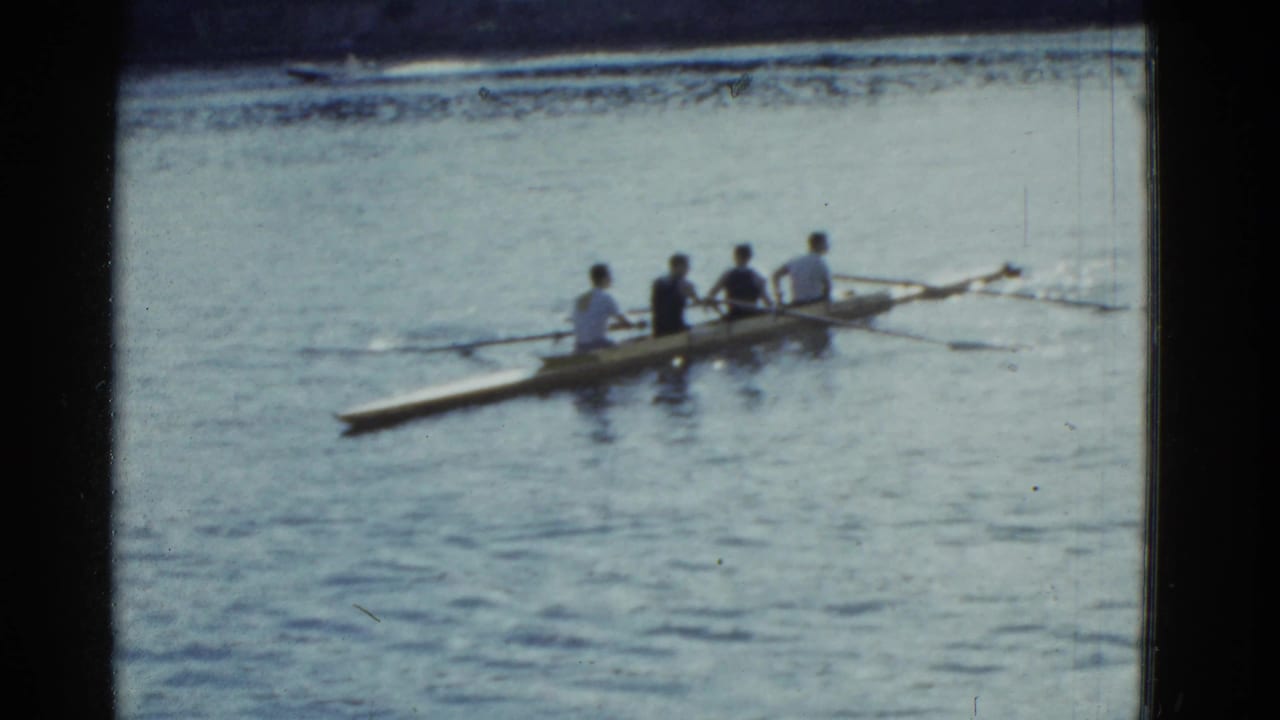 A four-person rowing crew glides on the river with oars in the water.