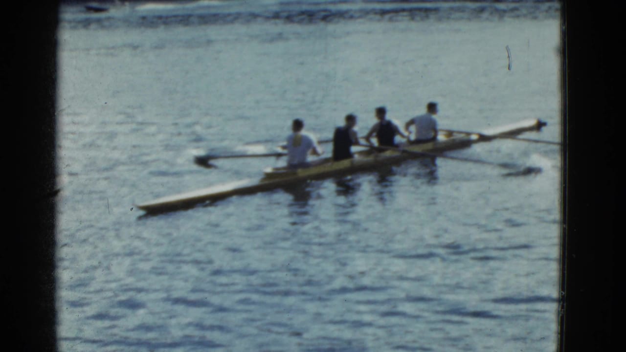 A rowing shell with four seated men moves across rippled blue water.