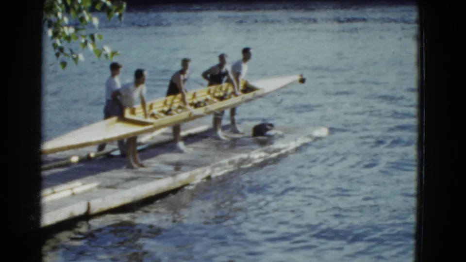 Men hold a long rowing shell on a waterfront dock, with the supplied metadata placing the scene in Boston in 1951.