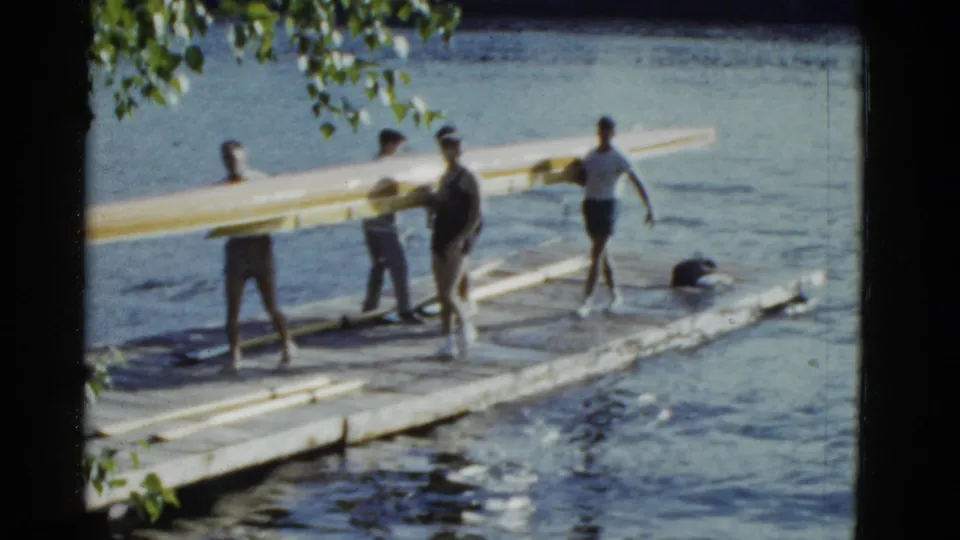 The group continues carrying the long wooden boat along the lakeside dock in faded 1951 8mm color footage.