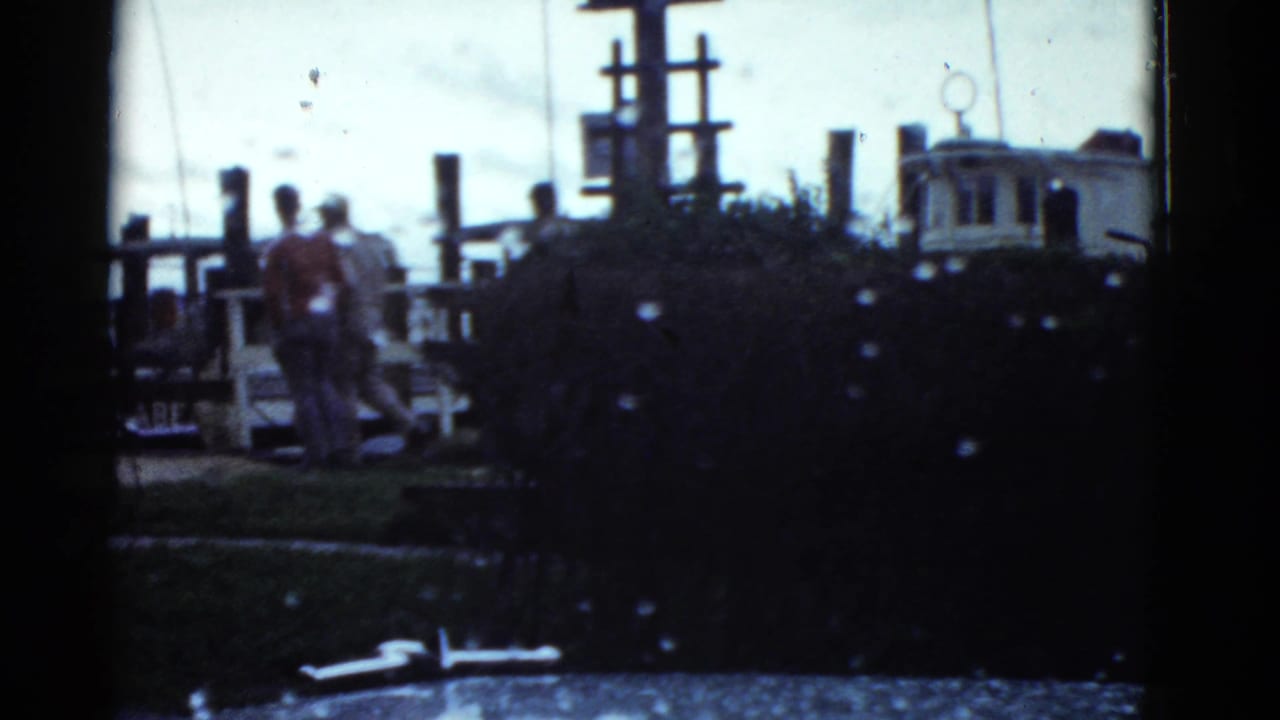 1951 Boston dockside home-movie frame showing several men near wooden pilings and small harbor craft.